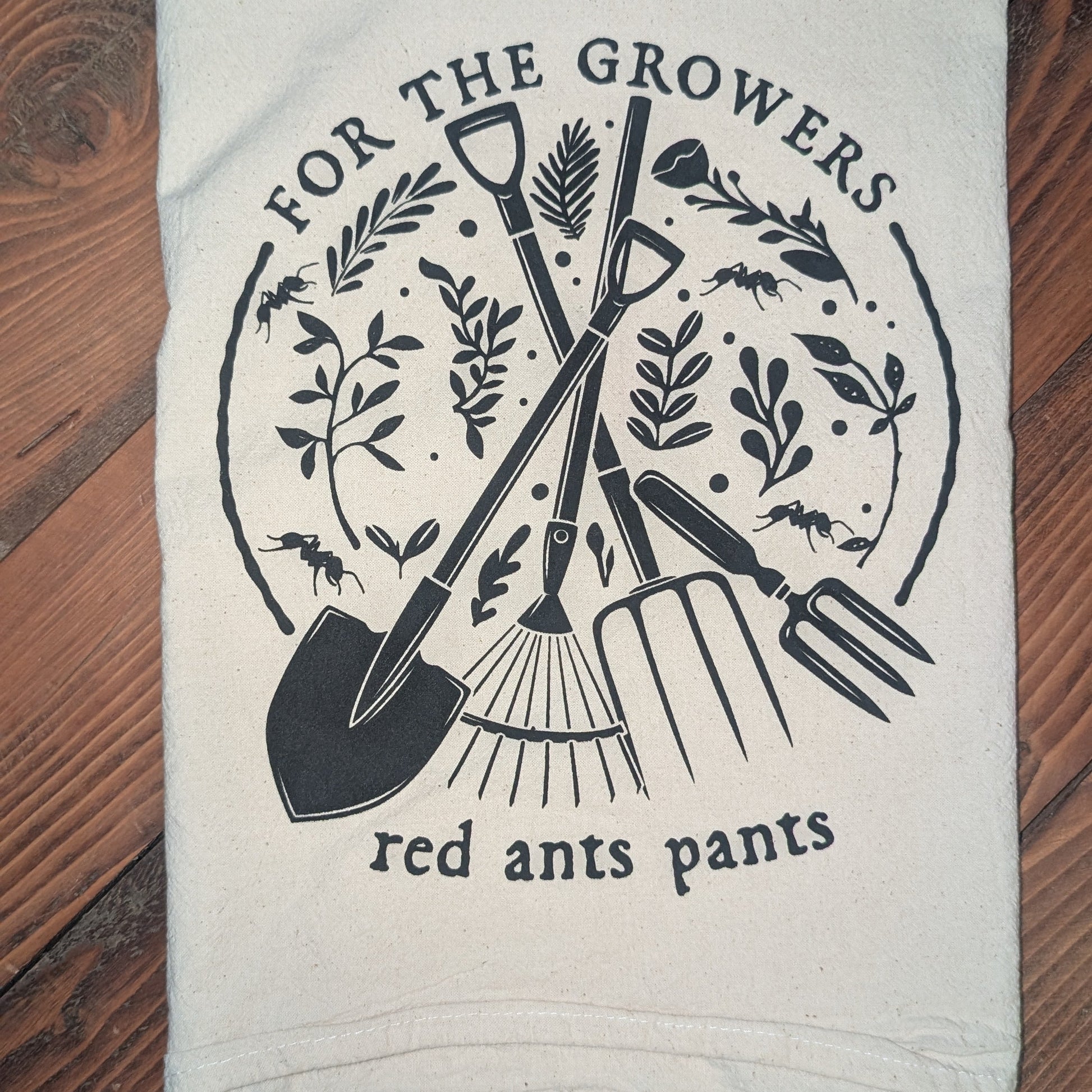 White towel with black gardening-themed design and text on a wooden surface