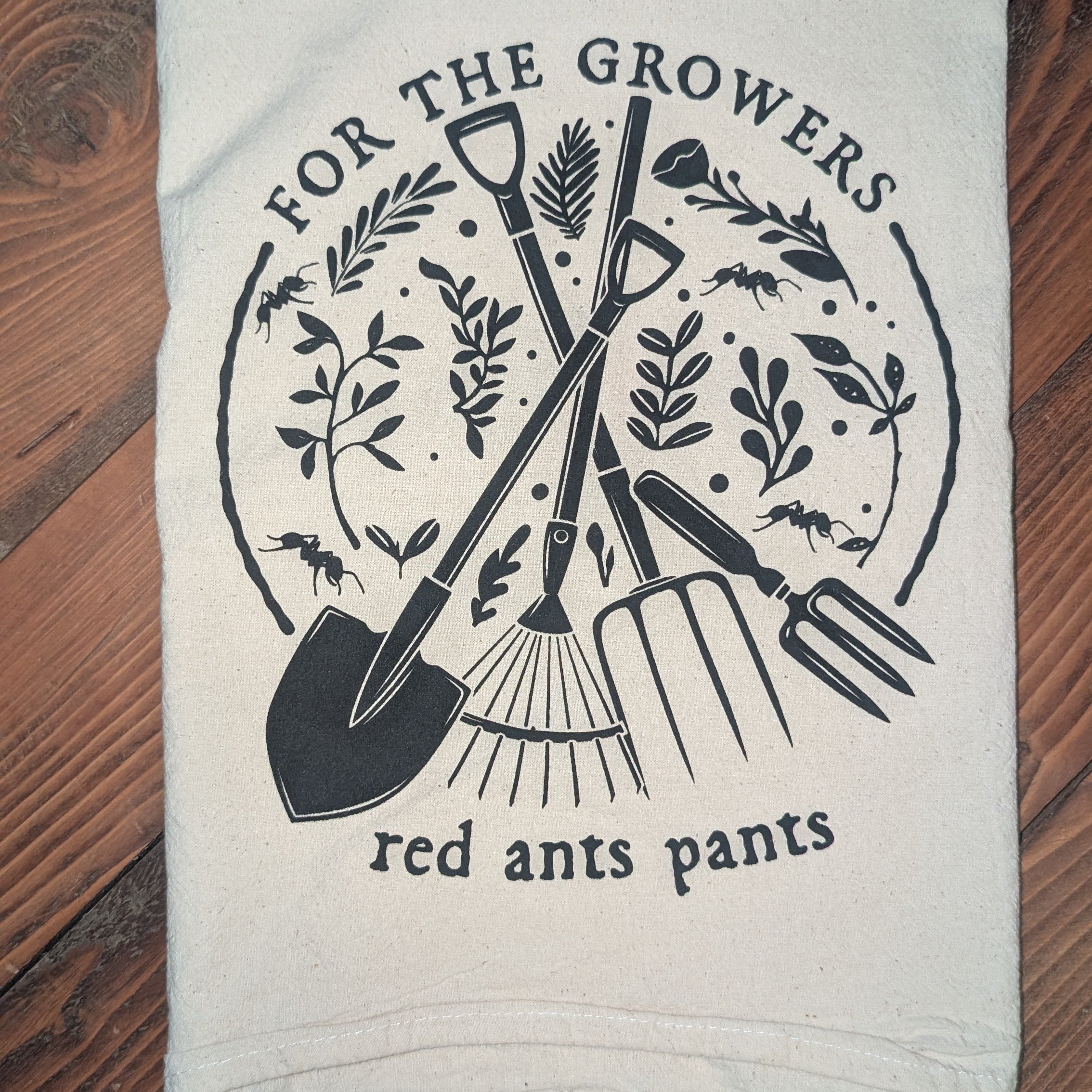 White towel with black gardening-themed design and text on a wooden surface