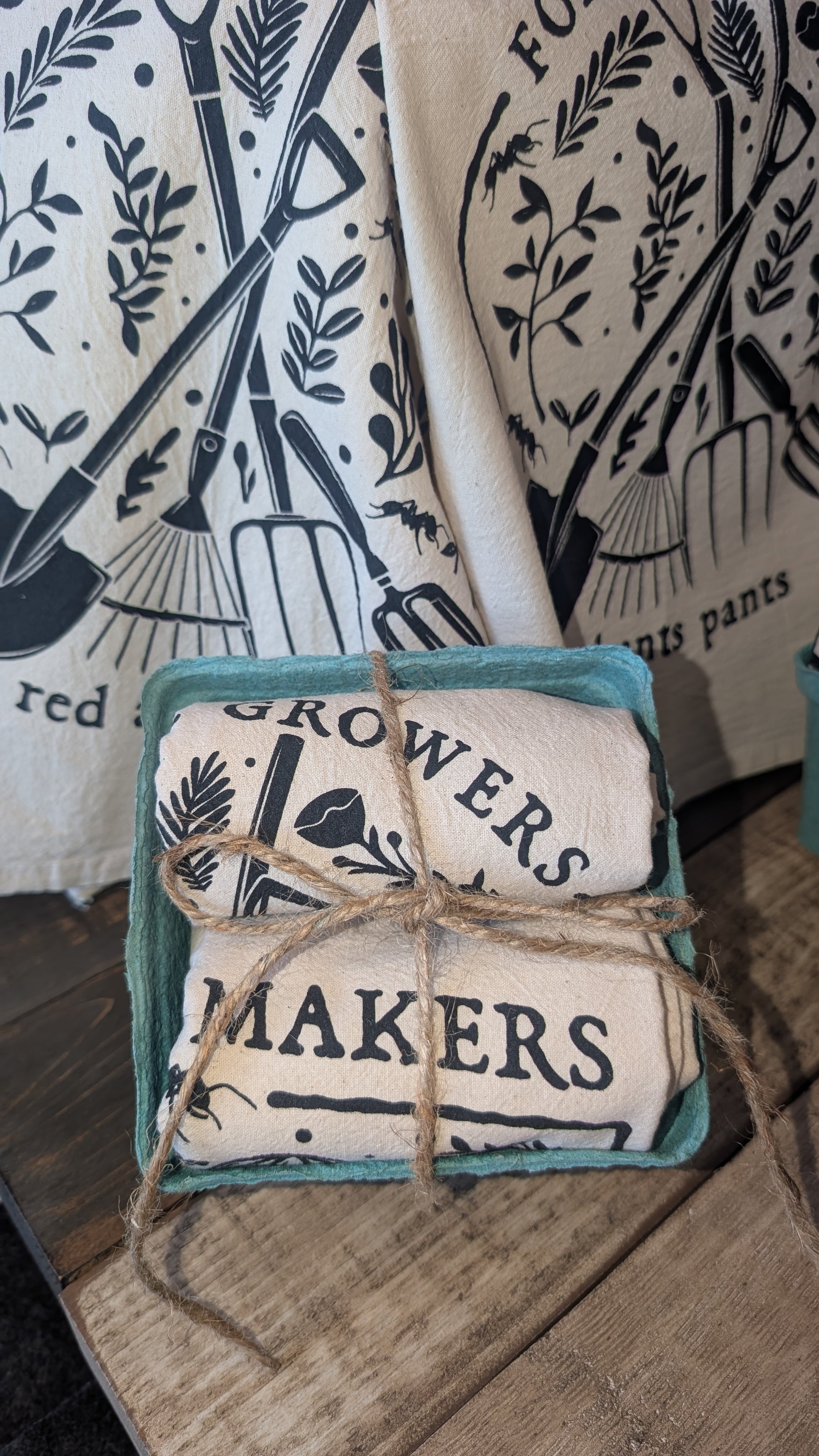 A bundle of two fabric towels with 'Growers' and  'Makers' text in a green box on a wooden surface.
