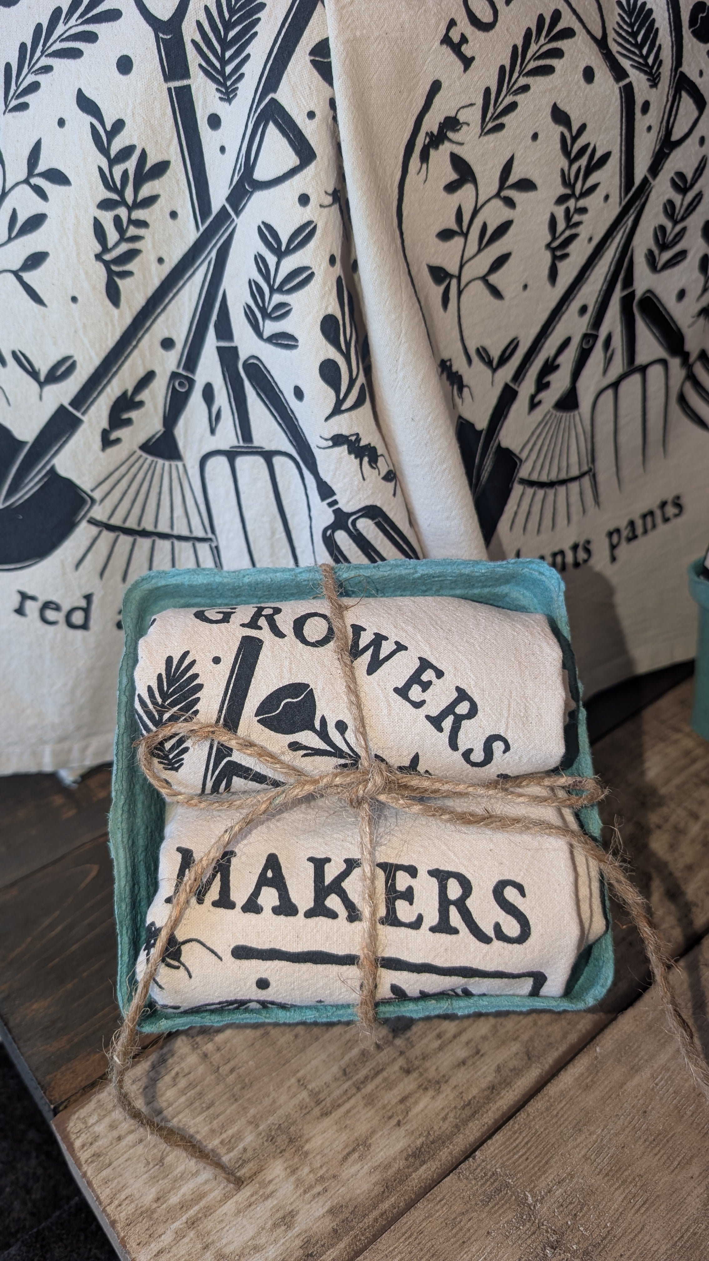 A bundle of two fabric towels with 'Growers' and  'Makers' text in a green box on a wooden surface.