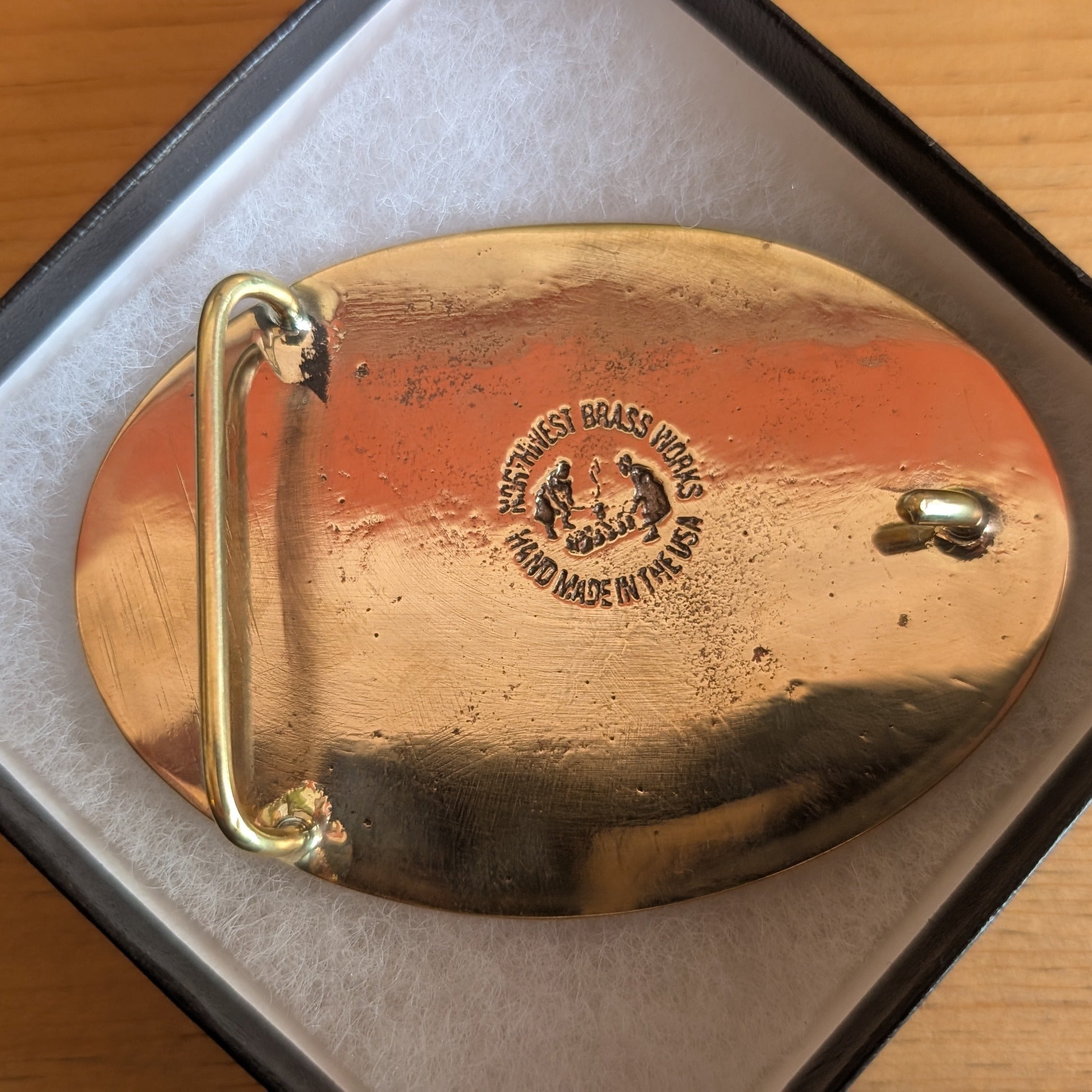 The back of a brass belt buckle with makers engraved design on a wooden surface