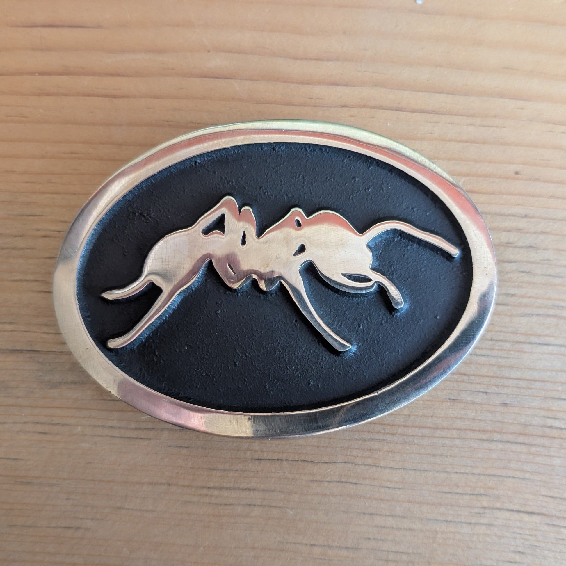 Brass metal belt buckle with an ant design on a wooden surface